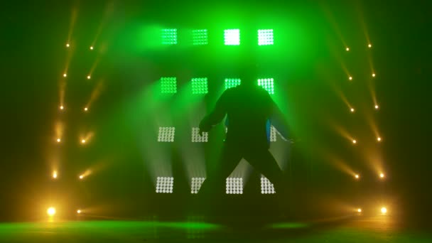 Silhouette of a talented young hip hop dancer. Hip hop street dance on a stage in dark studio with smoke and neon lighting. Dynamic lighting effects. Creative skills. Slow motion. — Stock Video