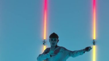 Dövmeli şık genç adam, parlak neon ışıkların önünde sokak dansı yapıyor. Hip hop tekniği öğretme konsepti. Gençlik alt kültürü. Çağdaş koreografi. Kapatın. Yavaş çekim