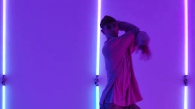 Dans eden genç yetenekli sokak dansçısı serbest stil hip hop hareketleri yapıyor. Parlak neon ışıklara karşı. Modern bir dans deyiminin tadını çıkaran bir sokak dansçısına yakın çekim. Yavaş çekim.