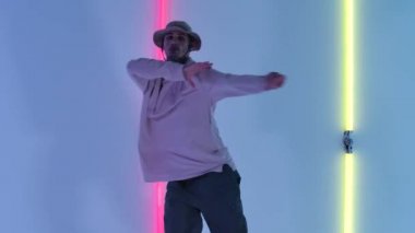 Dövmeli genç yakışıklı stüdyodaki parlak neon ışıkların arka planında hip hop dansı yapıyor. Profesyonel erkek dansçı serbest stil dansının tadını çıkarırken tek başına antrenman yapıyor. Kapatın. Yavaş çekim.