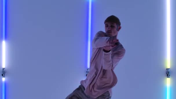 Cool young talented hip hop guy is dancing against the backdrop of bright neon lights, performing amazing gestures and movements. Street dance. Close up. Slow motion. — Stock Video