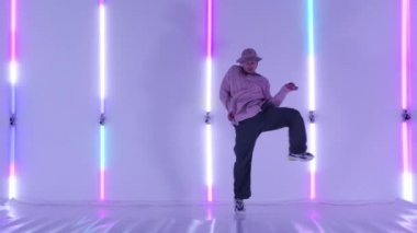 Dans eden genç yetenekli sokak dansçısı serbest stil hip hop hareketleri yapıyor. Parlak neon ışıklara karşı. Sokak dansçısı modern bir dans ifadesinin tadını çıkarıyor. Yavaş çekim.