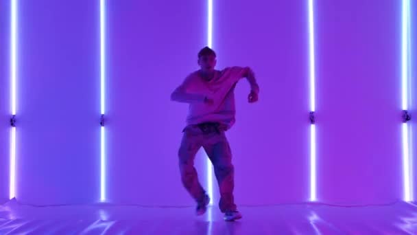 Dövmeli şık genç adam, parlak neon ışıkların önünde sokak dansı yapıyor. Hip hop tekniği öğretme konsepti. Gençlik alt kültürü. Çağdaş koreografi. Yavaş çekim. — Stok video
