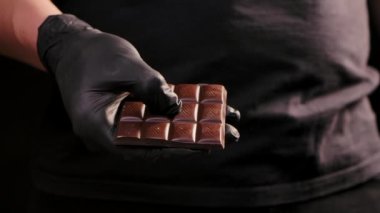 Siyah eldivenli şef çikolatayı ikiye bölerek eritiyor ve tatlı yapıyor, tatlı tatlılar pişiriyor. Erkek elleri yakın. Yavaş çekim.