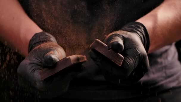 Mannen met zwarte handschoenen die chocola breken. Een donkere chocoladereep die doormidden breekt. Zoet ingrediënt voor het toetje. Sluit maar af. Langzame beweging. — Stockvideo
