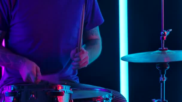 Drummer slaat drumbekkens met drumstokken in een donkere studio tegen de achtergrond van neonbuizen. De camera beweegt van de muzikanten handen op zijn gezicht en rug. Langzame beweging. Sluiten.. — Stockvideo