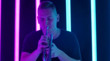 Stüdyoda bir adam pembe ve mavi neon tüplere karşı trompet çalar. Pipoda klasik performans. Ağır çekim. Kapat..