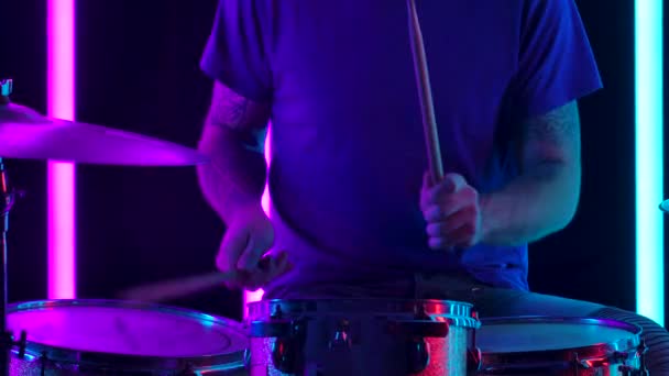 Skilled man muzikant speelt hedendaagse drumstel in een donkere studio verlicht door blauw en roze neon buizen. Close-up van een drummers getatoeëerde handen slaan drums met houten stokken. Langzame beweging. — Stockvideo