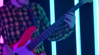 Adam gitar çalıyor. Bir gitaristin, neon ışıkta telleri parmaklayan elini kapat. Gitaristlerin ellerinden yüzüne doğru kamera hareketi. Yavaş çekim.