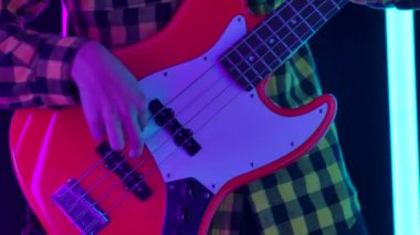 Ekose gömlekli bir müzisyen, stüdyoda mavi ve pembe neon tüplerin arka planına karşı gitar çalar. Telleri geren bir adamın ellerine ve bir gitarın boynuna yaklaş. Yavaş çekim.