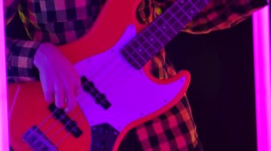 Ekose gömlekli bir müzisyen stüdyoda çok renkli neon borularla çevrili bir konser programını prova ediyor. Telleri geren bir adamın ellerine ve bir gitarın boynuna yaklaş. Yavaş çekim.