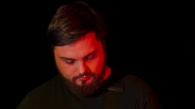 Bir grup gitarist, enstrümanlarıyla birlikte stüdyoda neon ışıkta siyah bir arkaplana karşı beste yapıyor. Ağır çekim. Kapat..