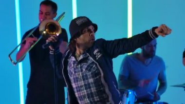 Bir konser rock grubu stüdyoda bir şarkıcı, trombon ve davulcuyla neon boruların arka planına karşı konser verir. Kamera, şarkıcının yüzünden ayaklarına kadar hareket ediyor. Kapatın. Yavaş çekim.
