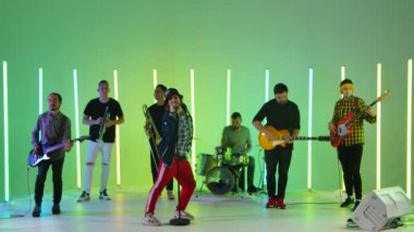 Müzik grubu ska punk, stüdyoda reggae 'yi çok renkli neon tüplerin arka planına karşı çalıyor. Enerjik müzik ve dans. Ağır çekim. Kapat..