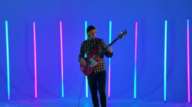 Müzisyen, stüdyodaki çok renkli neon boruların arka planına karşı beyaz kırmızı bir elektro gitarda solo çalıyor. Parti, müzik festivali, konser. Yavaş çekim.