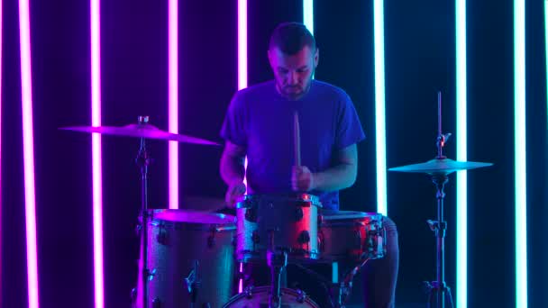 Der Schlagzeuger spielt meisterhaft das Schlagzeug. Ein Musiker spielt im Studio vor dem Hintergrund pinkfarbener und blauer Neonröhren in Zeitlupe ein Solo. Nahaufnahme. — Stockvideo