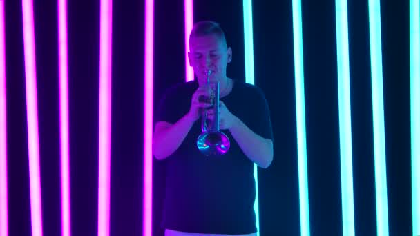 Un uomo suona la tromba in studio su uno sfondo di tubi al neon rosa e blu. Classica performance sul tubo. Al rallentatore. Da vicino.. — Video Stock