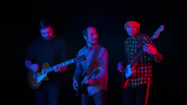 三位吉他手在霓虹灯下的黑色背景下，在工作室的乐器上表演作曲。慢动作靠近点. — 图库视频影像
