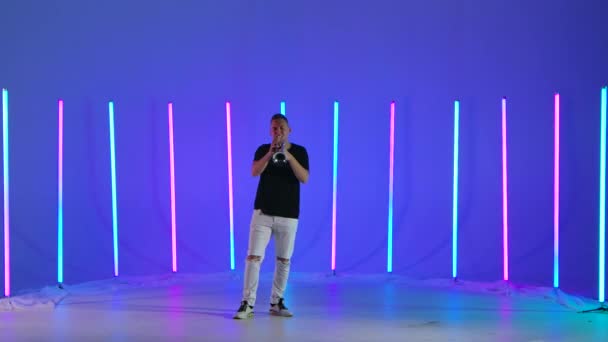Solo performance of a musician trumpeter in the studio against the background of multicolored neon lights. The man plays his trumpet masterly. Slow motion. — Stock Video
