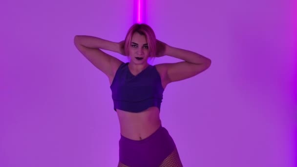 Sexig ung kvinna dansar twerk. Sensuell kvinna i korta shorts flyttar sin kropp och twerkar mot bakgrund av ljusa neonljus i studion. Närbild. Långsamma rörelser. — Stockvideo