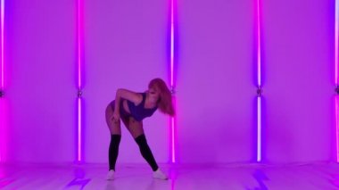 Sensual, sexy dancing young woman with pink hair in the studio. Slow motion female dancer dancing twerk, shaking her butt against the backdrop of bright neon lights.