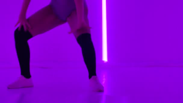 Mulher com danças de cabelo rosa twerk em luzes de néon ultravioleta realizando belos truques complexos no chão. Dança do espólio. Rabos sensuais. Sedução. Vida nocturna. Movimento lento. Fechar. — Vídeo de Stock