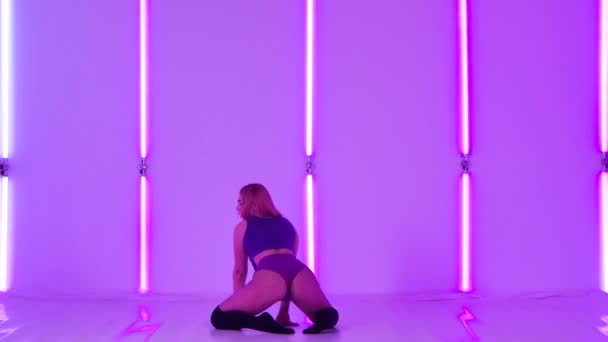 Sexy female dancer in short shorts is dancing twerk on the floor. Sensual young woman twerking her buttocks in the studio against a background of bright neon lights. Slow motion. — Stock Video