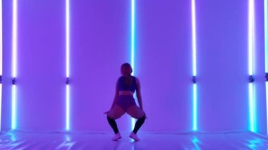 Professional dancer with an attractive body shakes her ass and jumps. Sensual twerk dance performed by a pretty woman against the backdrop of bright neon lights. Erotic booty movements. Slow motion.