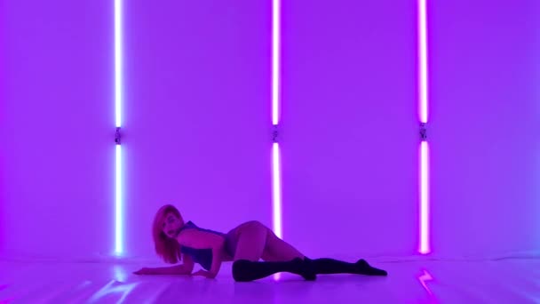 Attraente donna sexy in un crop top, calzini al ginocchio e pantaloncini ballare e scuotere il suo bottino chic mentre sdraiato sul pavimento. Booty danza in studio con luci al neon viola brillante. Rallentatore. — Video Stock