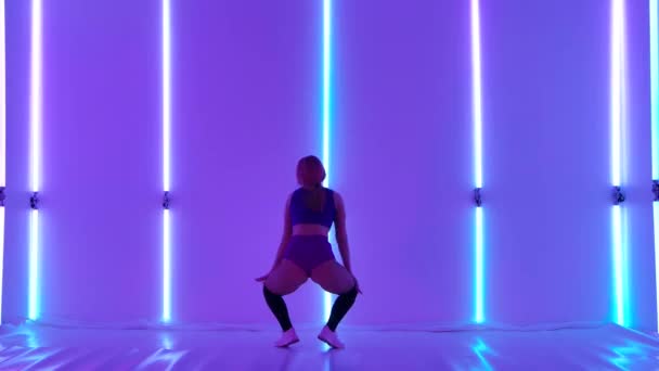 Professional dancer with an attractive body shakes her ass and jumps. Sensual twerk dance performed by a pretty woman against the backdrop of bright neon lights. Erotic booty movements. Slow motion. — Stockvideo