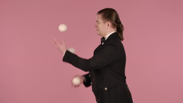 Hombre malabarista muestra trucos con bolas blancas, lanzando y la captura de ellos. Un artista de circo profesional realiza un programa de espectáculos en un fondo de estudio rosa. Aislado de cerca. Movimiento lento. — Vídeos de Stock