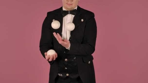 Man jonglör visar tricks med vita bollar, kastar och fånga dem. En professionell cirkusartist utför ett showprogram på en rosa studiobakgrund. Isolerad på nära håll. Långsamma rörelser. — Stockvideo