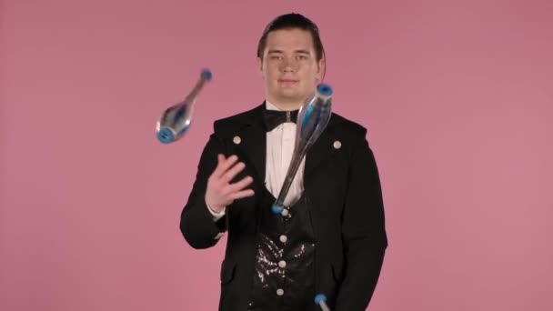 Le jongleur utilise des clubs jonglant en studio sur fond rose. Un homme élégant en costume noir lance et attrape habilement les épingles. Ferme là. Mouvement lent. — Video