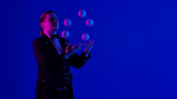 Joven hombre con estilo hace malabares con cinco bolas blancas al mismo tiempo. Una actuación virtuosa de un artista de circo en un estudio oscuro. Pantalla azul, tecla de croma. De cerca. Movimiento lento. — Vídeo de stock