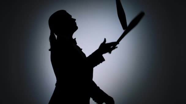 Side view black silhouette of man juggling with pins in the spotlight. Circus performer with an entertaining show program. Monochrome background is illuminated with studio light. Close up. Slow motion — Stock Video