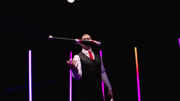 Kör mozgás kamera körül professzionális cirkusz előadóművész forgó csapok egy fekete stúdió háttér közepette fényes neon fények. Orbitális lövés közelről. Lassú mozgás.. — Stock videók