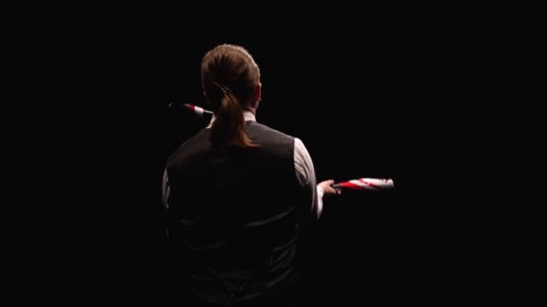 Camera rotates around concentrated man professionally juggling and balancing pins. Juggler shows tricks on a black studio background. Orbital shot close up. Slow motion. — Stock Video