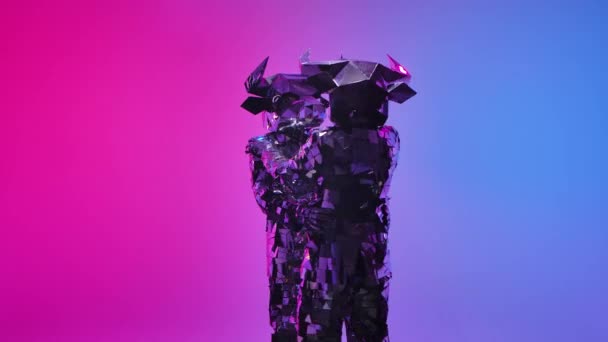 Des cyber-gens miroirs en costumes brillants de taureaux à cornes dansent s'embrassant sur fond studio bleu néon rose. Symbole de 2021, le taureau, brille et se reflète dans la lumière. Mouvement lent — Video