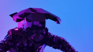 Parlak aynalı kostümlü, boğa kafalı ve boynuzlu iki aktör festival partisinde dans ediyor. Karanlık bir stüdyoda renkli pembe neon ışıkların arka planında yansıyan insanları göster. Kapat..