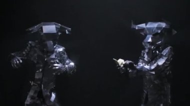 Aynadan parlayan gümüş kostümlü dansçılar dumanlı stüdyo arka planında boynuzlu boğa şeklinde. Oyuncular dans eder ve siyah arka plana dolar saçar. Kapatın. Yavaş çekim.