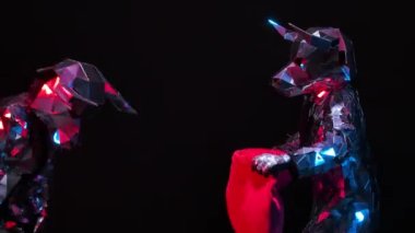 Actors in shiny costumes of bulls from mirrors playfully have fun and butt horns on a red rag. Bulls in reflective suits twinkle against a black studio background. Close up. Slow motion.