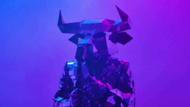 Shiny bull in costume made of mirrors singing and dancing near retro microphone on neon blue pink studio background. Symbol of 2021, bull, shines and is reflected in club lights. Close up. Slow motion — стоковое видео