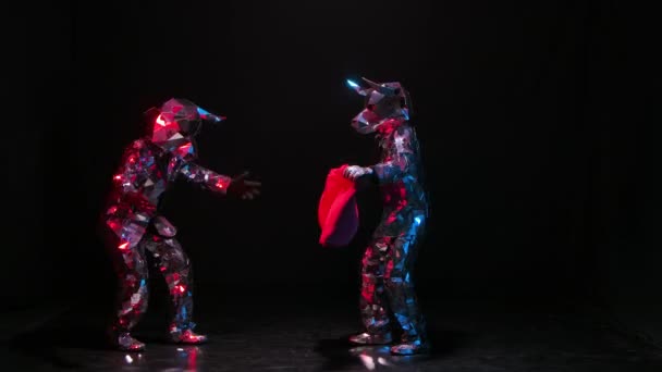 Actors in shiny costumes of bulls from mirrors playfully have fun and butt horns on red rag. Bulls in reflective suits twinkle in beams of colored lights against black studio background. Slow motion. — Video Stock