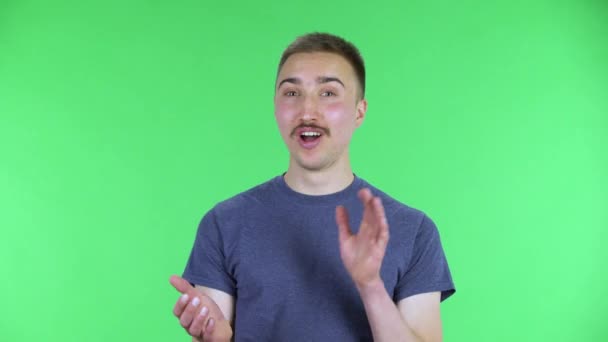 Портрет молодого чоловіка, який дивиться на камеру, стискаючи руки з захоплюючим виразом вау. Милий чоловік з вусами в синій футболці позує на зеленому екрані в студії. крупним планом . — стокове відео
