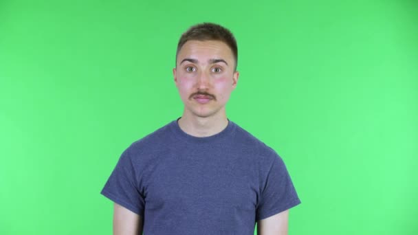 Porträt eines jungen Mannes, der mit einem Wow-Gesichtsausdruck in die Kamera blickt. Netter Mann mit Schnurrbart in blauem T-Shirt posiert auf einer grünen Leinwand im Studio. Nahaufnahme. — Stockvideo