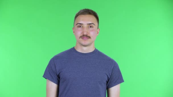 Портрет молодого чоловіка, який дивиться на камеру з захоплюючим виразом. Милий чоловік з вусами в синій футболці позує на зеленому екрані в студії. крупним планом . — стокове відео
