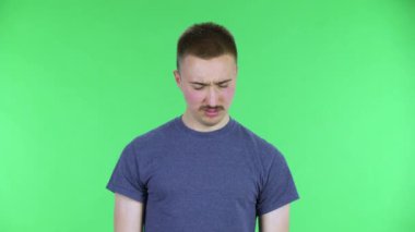 Genç bir adamın portresi soğuk algınlığı, boğaz ağrısı ve baş ağrısı, öksürük. Bıyıklı, mavi tişörtlü, stüdyoda yeşil ekranda poz veren yakışıklı bir erkek. Kapat..