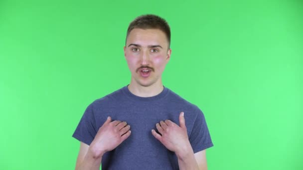 Retrato de um jovem apontando-se, dizer quem me não obrigado eu não preciso. Homem bonito com um bigode em uma camiseta azul posando em uma tela verde no estúdio. Fechar. — Vídeo de Stock