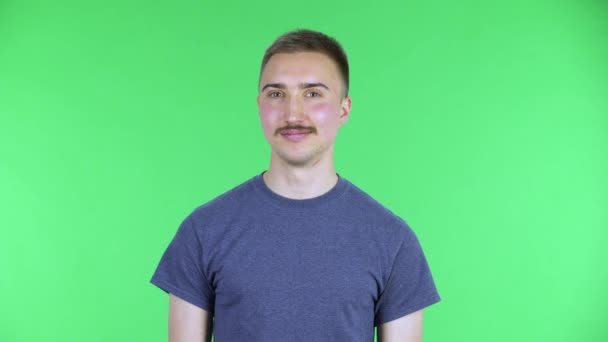 Porträt eines jungen Mannes, der breit lächelt und zwinkert. Netter Mann mit Schnurrbart in blauem T-Shirt posiert auf einer grünen Leinwand im Studio. Nahaufnahme. — Stockvideo