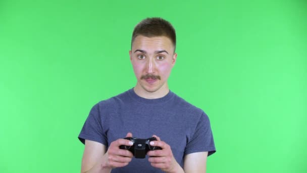 Portret młodego człowieka grającego w grę wideo za pomocą kontrolera bezprzewodowego i przegrywającego. Słodki mężczyzna z wąsami w niebieskiej koszulce, pozujący w studio na zielonym ekranie. Zamknij się.. — Wideo stockowe